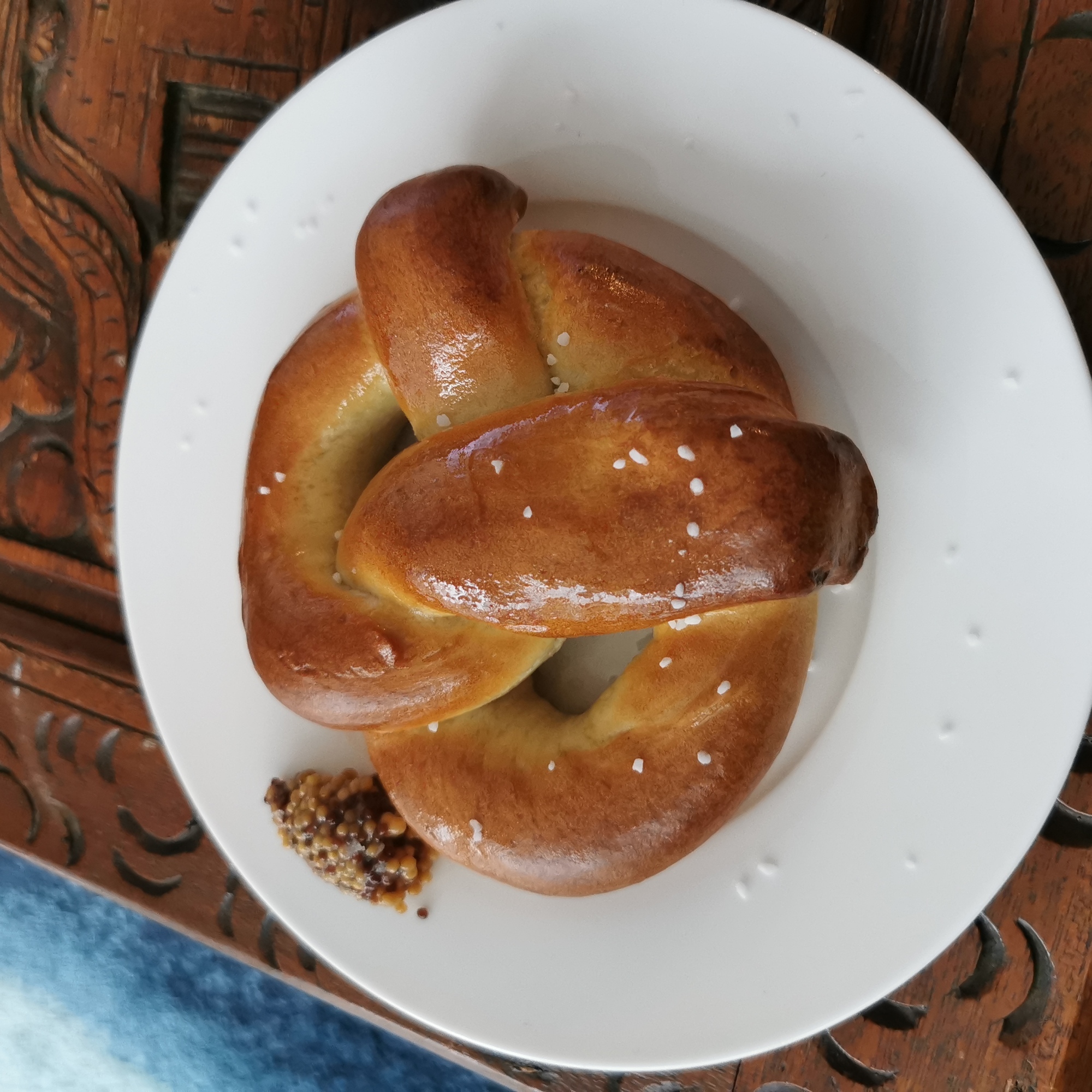 Freshly baked soft pretzel sits on a white plate with a dollop of seeded mustard